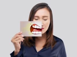 Asian woman in the dark blue shirt holding a paper with the periodontal and gingivitis cartoon picture of his mouth against the gray background, Decayed tooth, The concept with healthcare gums and teeth